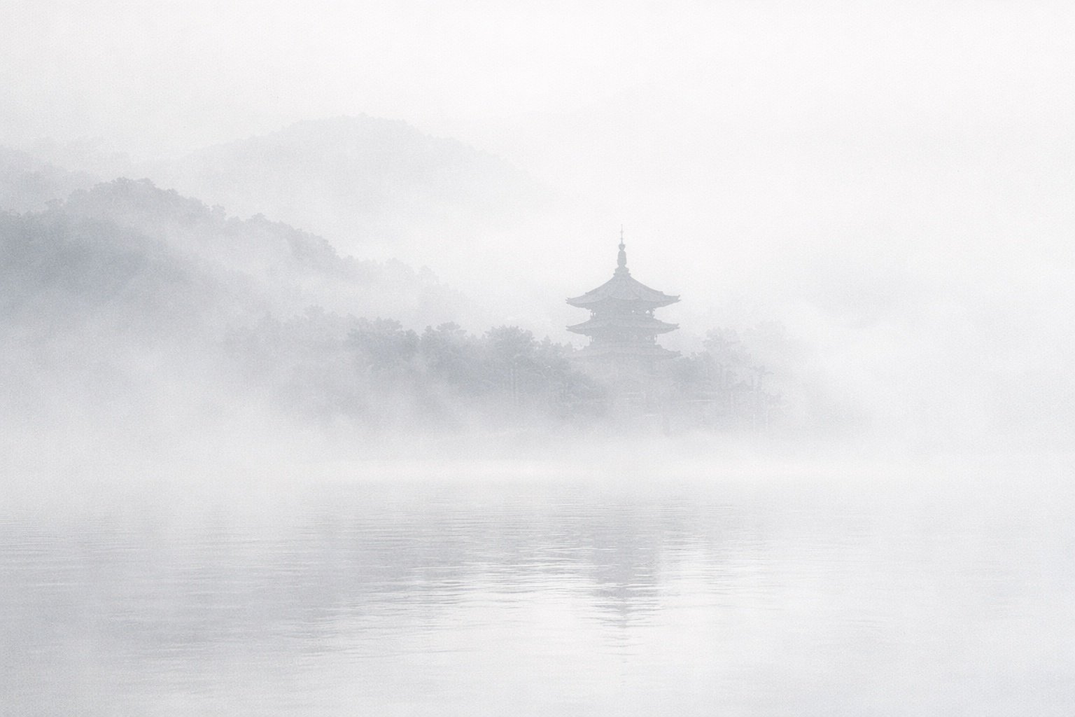 A distant temple almost disappearing into fog above still water.